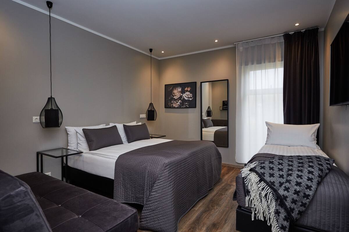 A modern hotel room with two beds, a large mirror, and a pendant light.