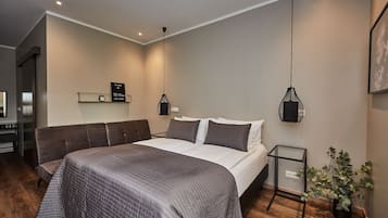 A modern hotel room with a large bed, a bedside table, a small desk, and a potted plant.