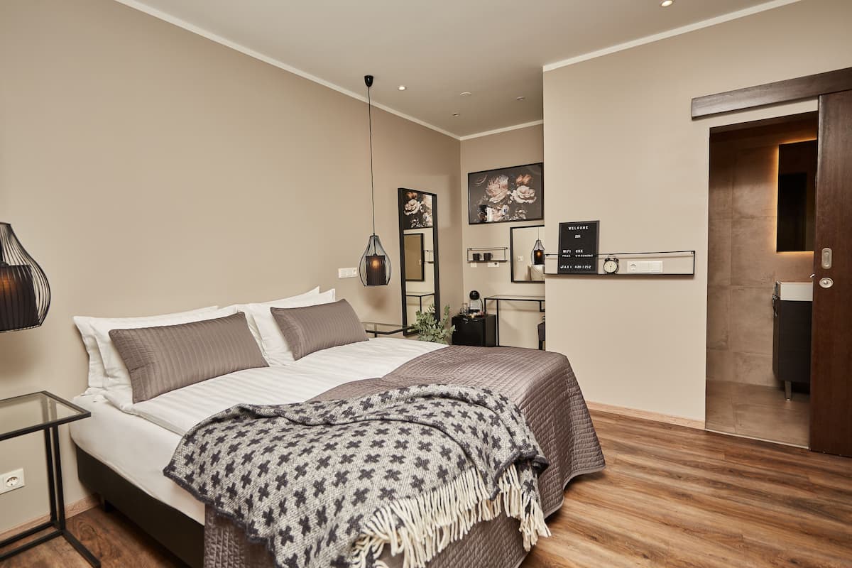 A modern hotel room with a bed, bedside table, lamp, and a door leading to the bathroom.