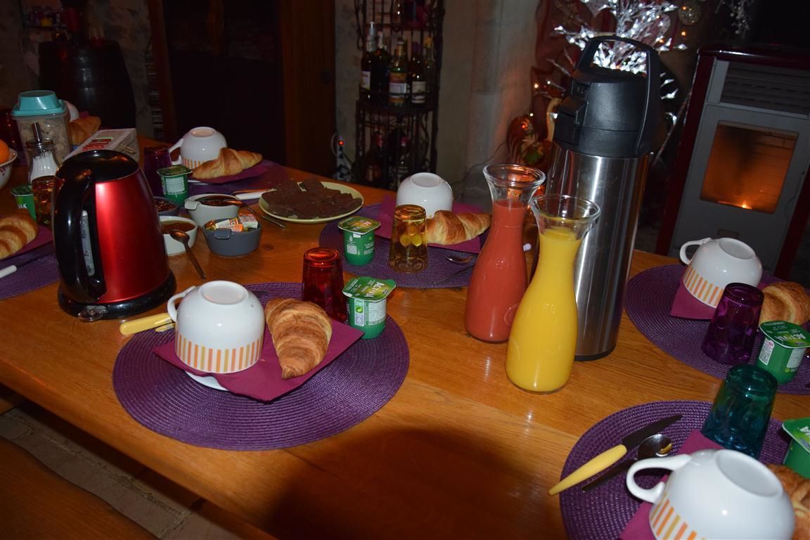 A breakfast table with croissants, a coffee pot, a juice pitcher, and various condiments.