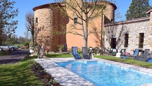 A swimming pool with lounge chairs, a stone building, and a car parked nearby.
