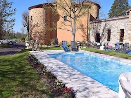 Una piscina con sillas de descanso, un edificio de piedra y un coche aparcado cerca.