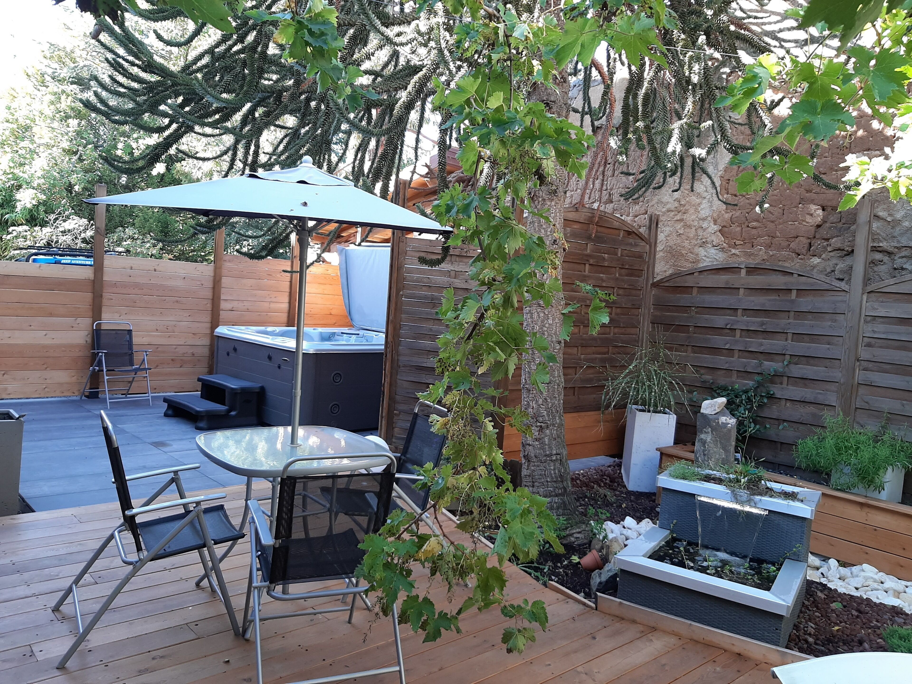 Une terrasse en bois avec un jacuzzi, un coin salon extérieur et une pergola dotée d’une table et de chaises.