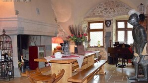A rustic interior with a stone wall, wooden furniture, a piano, and a knight statue.