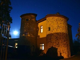 Un edificio de piedra con una torre redonda y una sección rectangular, iluminado por una luz cálida.