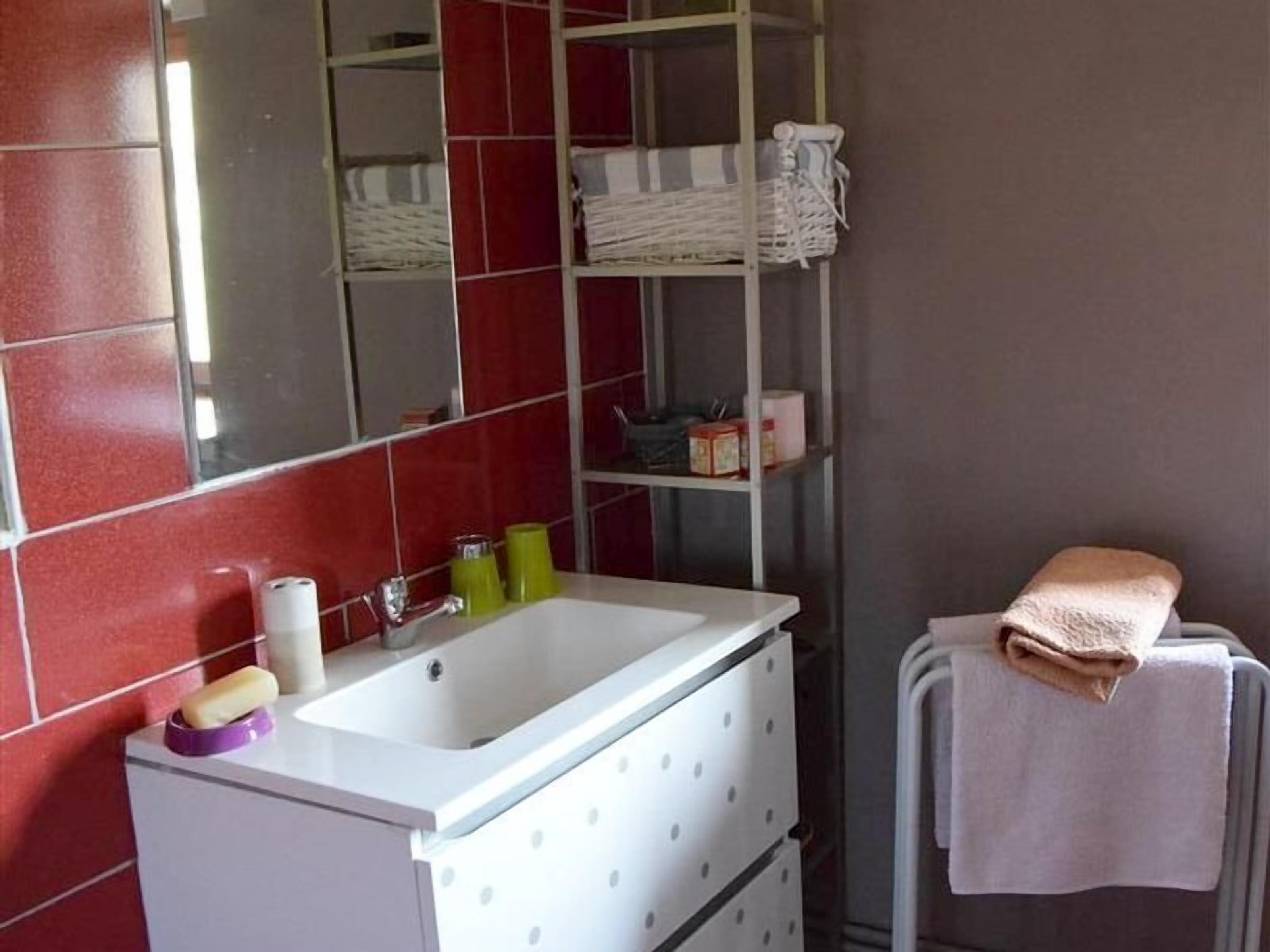 A bathroom with a white sink, red tiled walls, a mirror, and a towel rack.