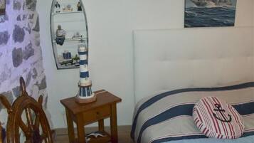 A bedroom with a bed, a wooden nightstand with a model ship, a wooden ship's wheel, and a painting of a sailing ship.
