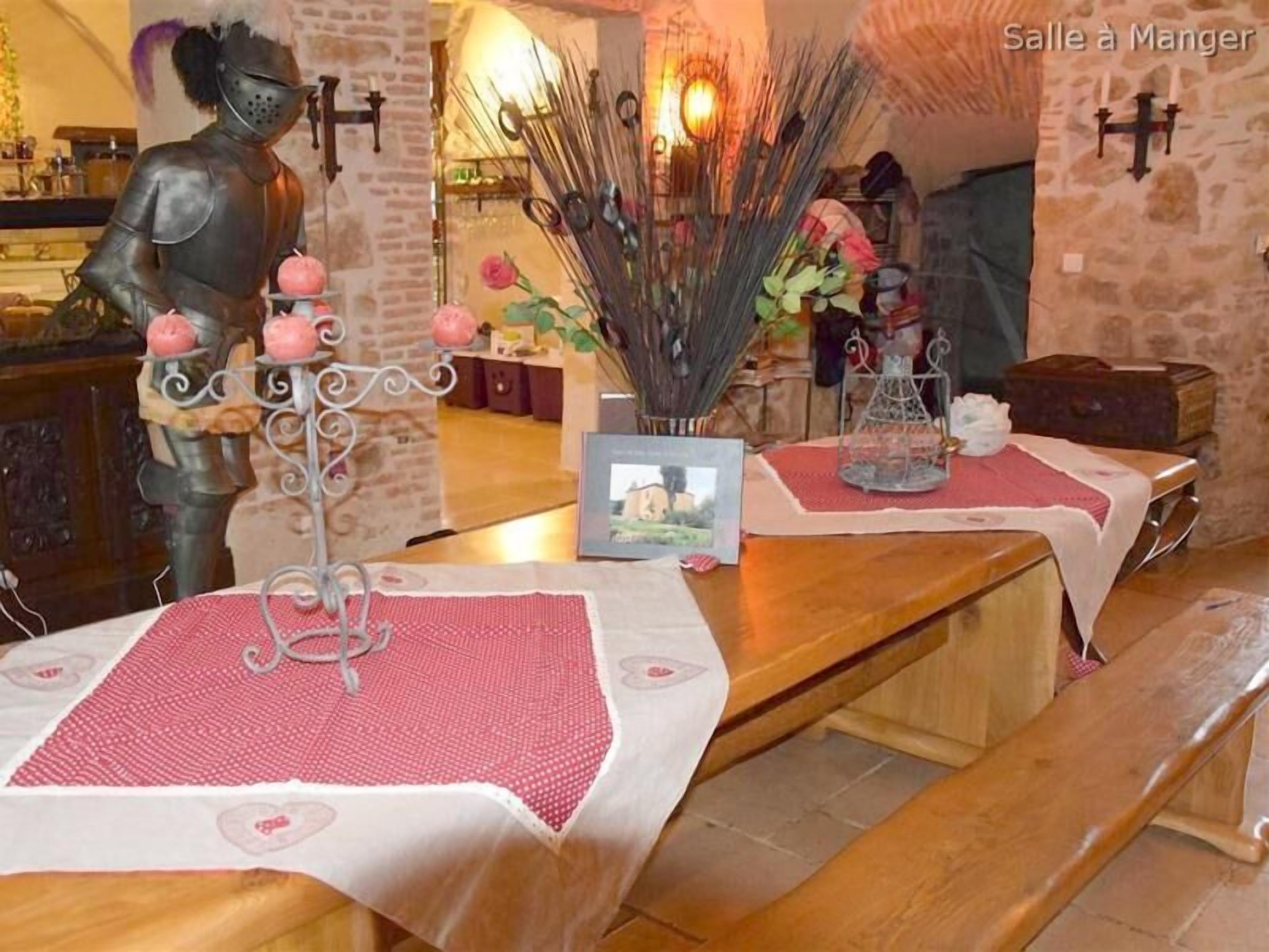 Ein Essbereich mit rustikaler Steinwand, einer Ritterstatue und einem Tisch, gedeckt mit einer roten Tischdecke und einer Blumenvase.