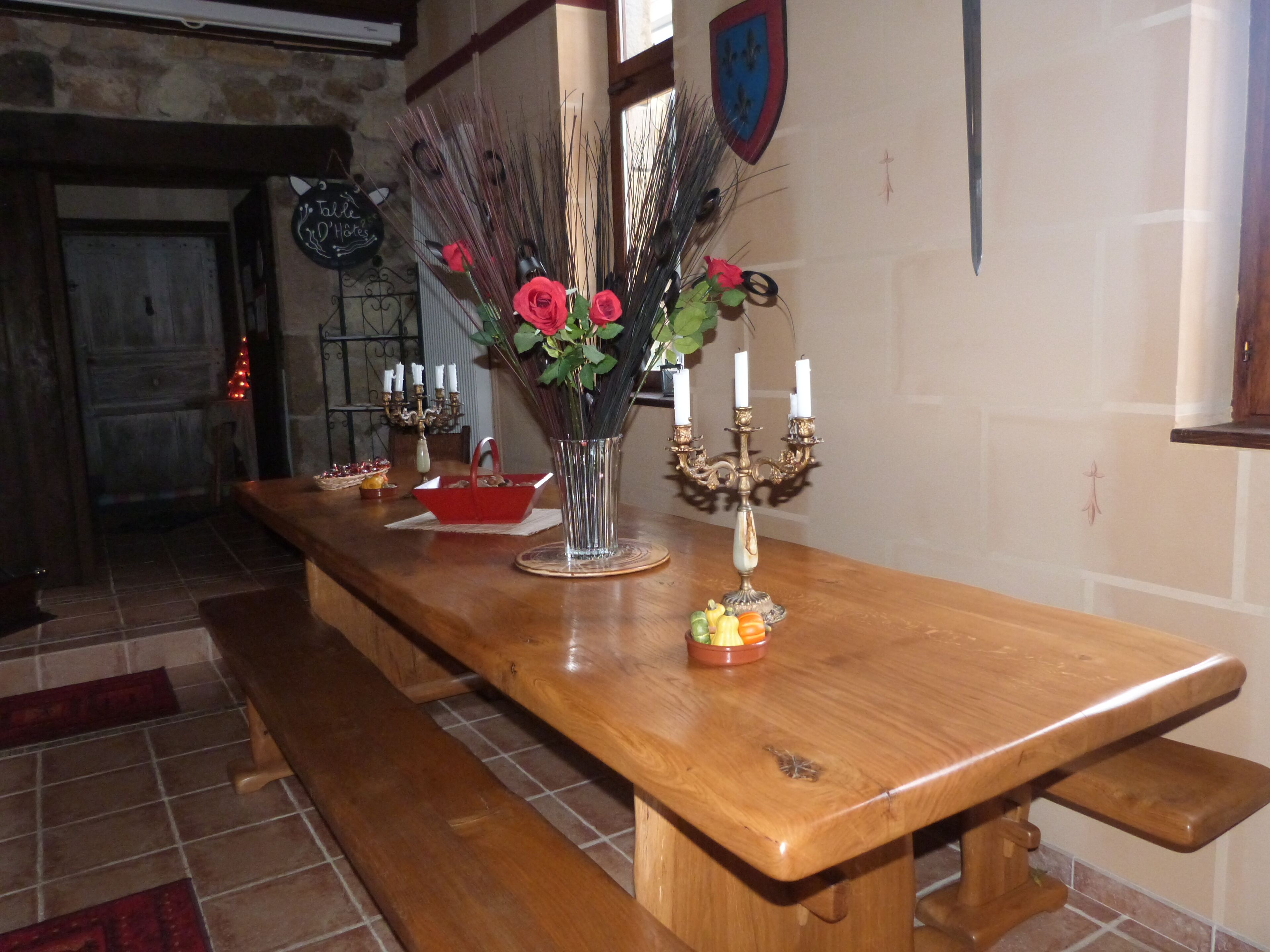 A wooden table with a vase of red flowers, a candle holder, and a small fruit bowl.