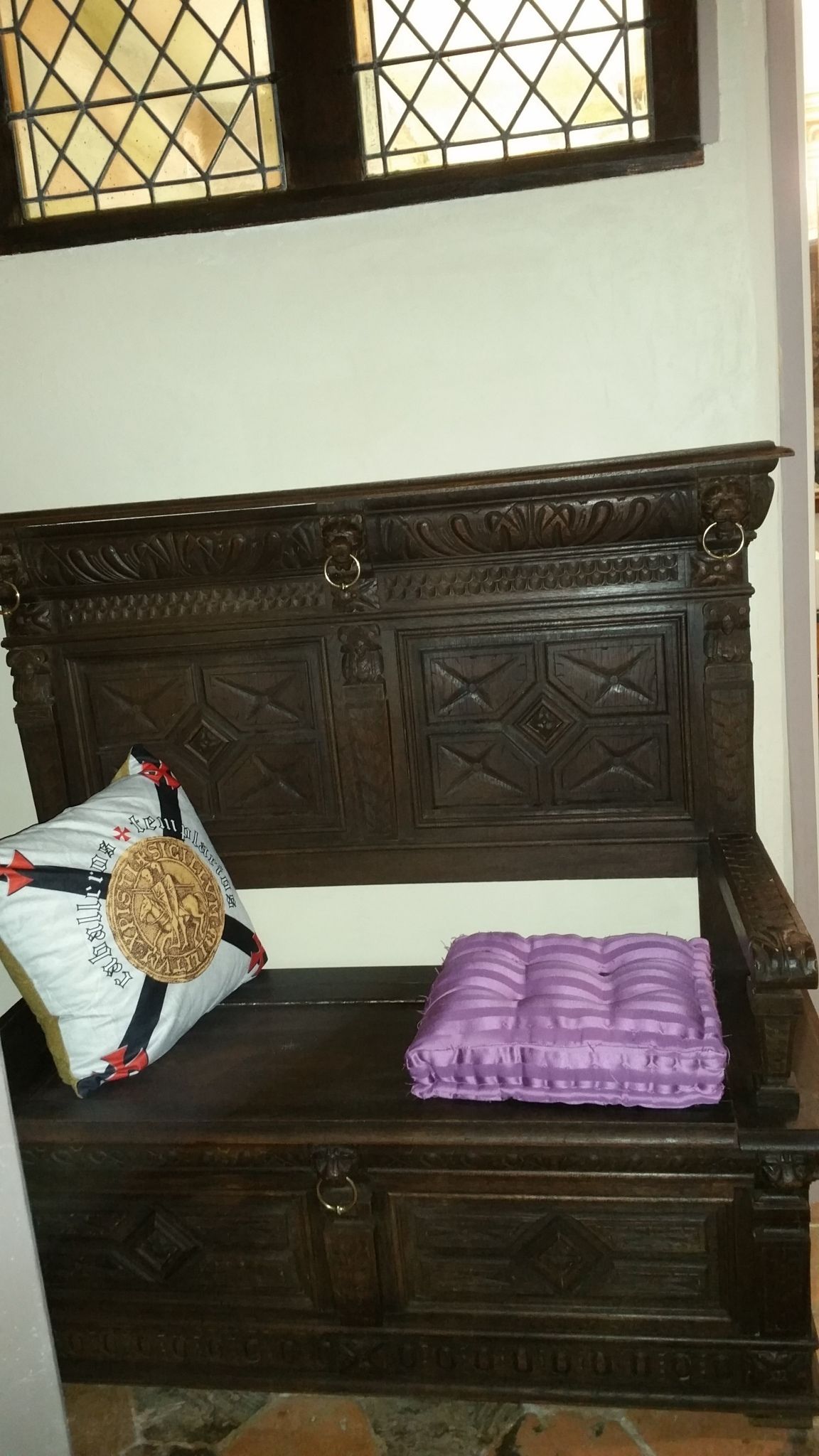 Un banco de madera con tallas elaboradas y un cojín.