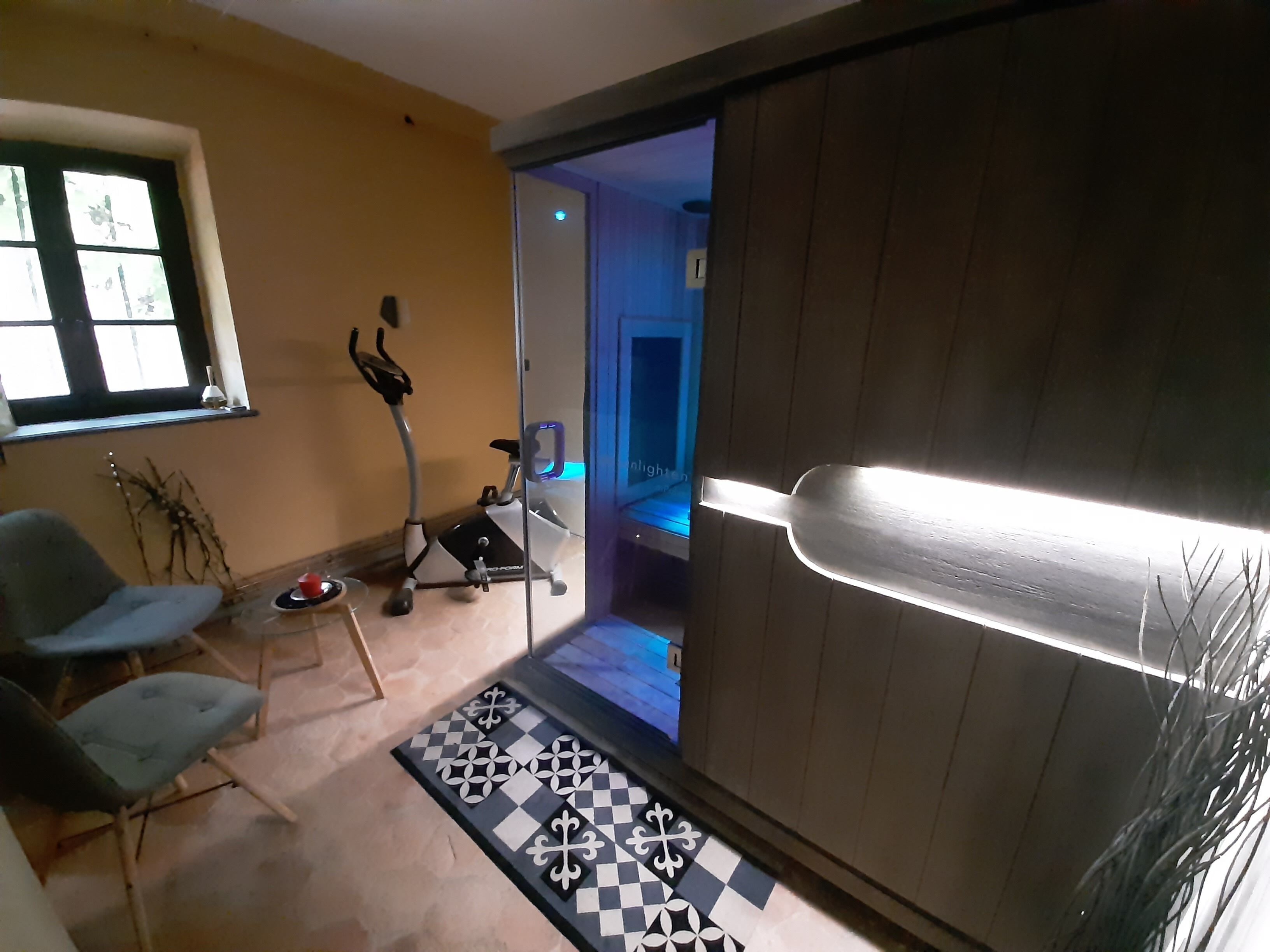A living room with a treadmill, a patterned rug, and a sliding door leading to another room.