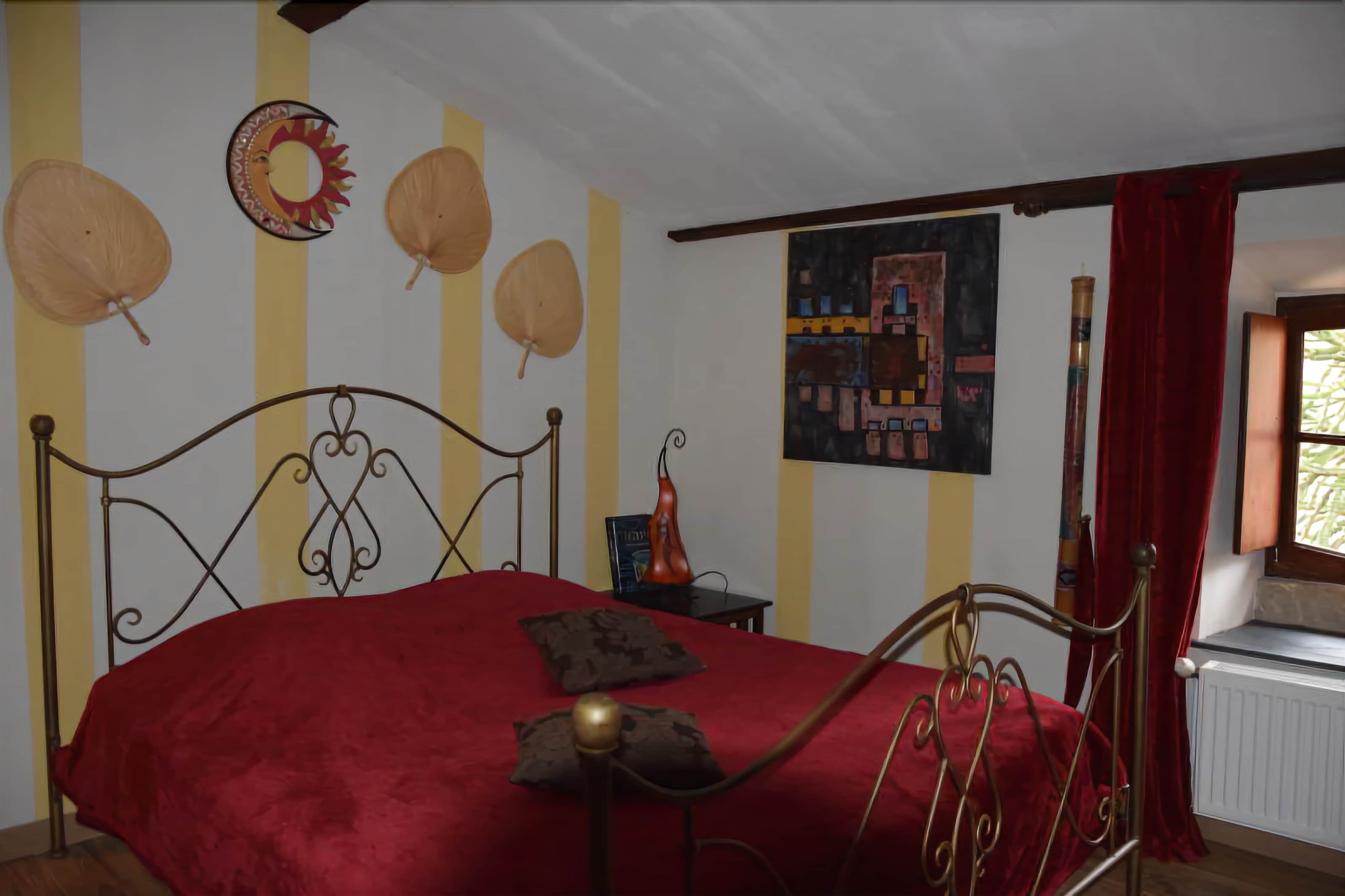 A bedroom with a metal bed frame, red bedding, and striped walls.