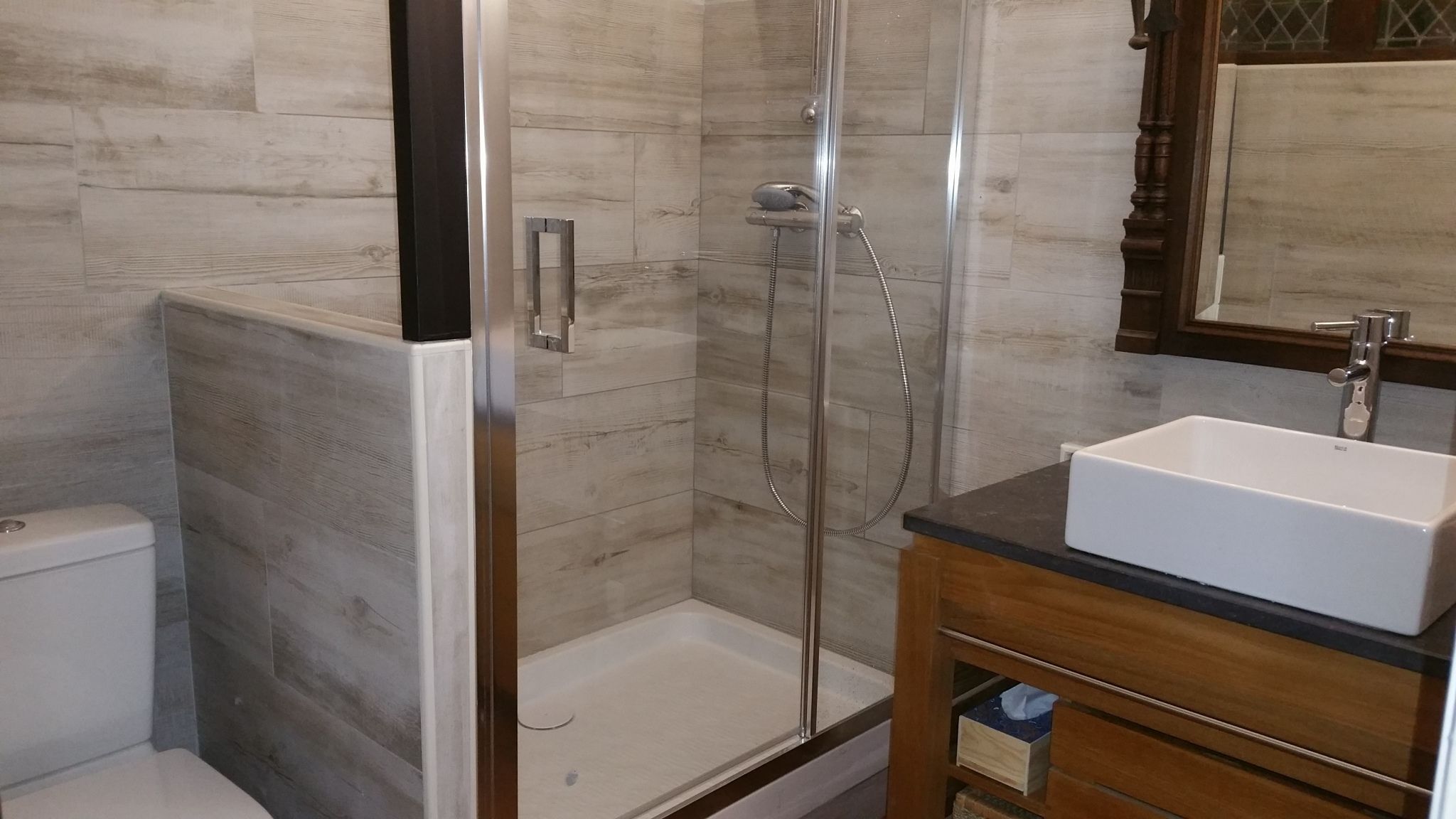 Un baño con ducha de vidrio, lavamanos blanco y tocador de madera.