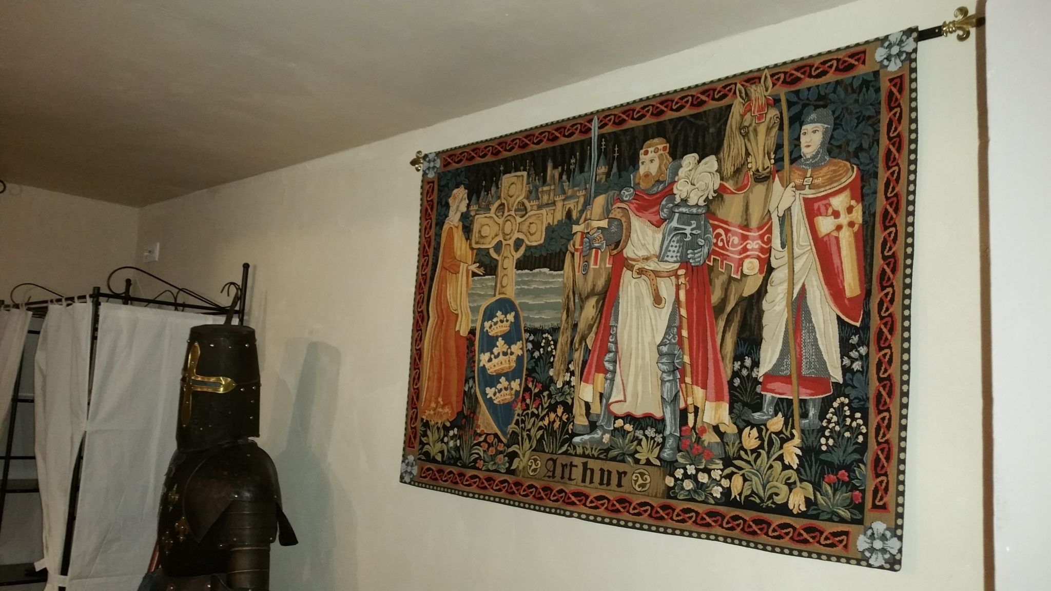 Une tapisserie médiévale sur laquelle on peut voir le nom « Arthur », un chevalier en armure et une croix.