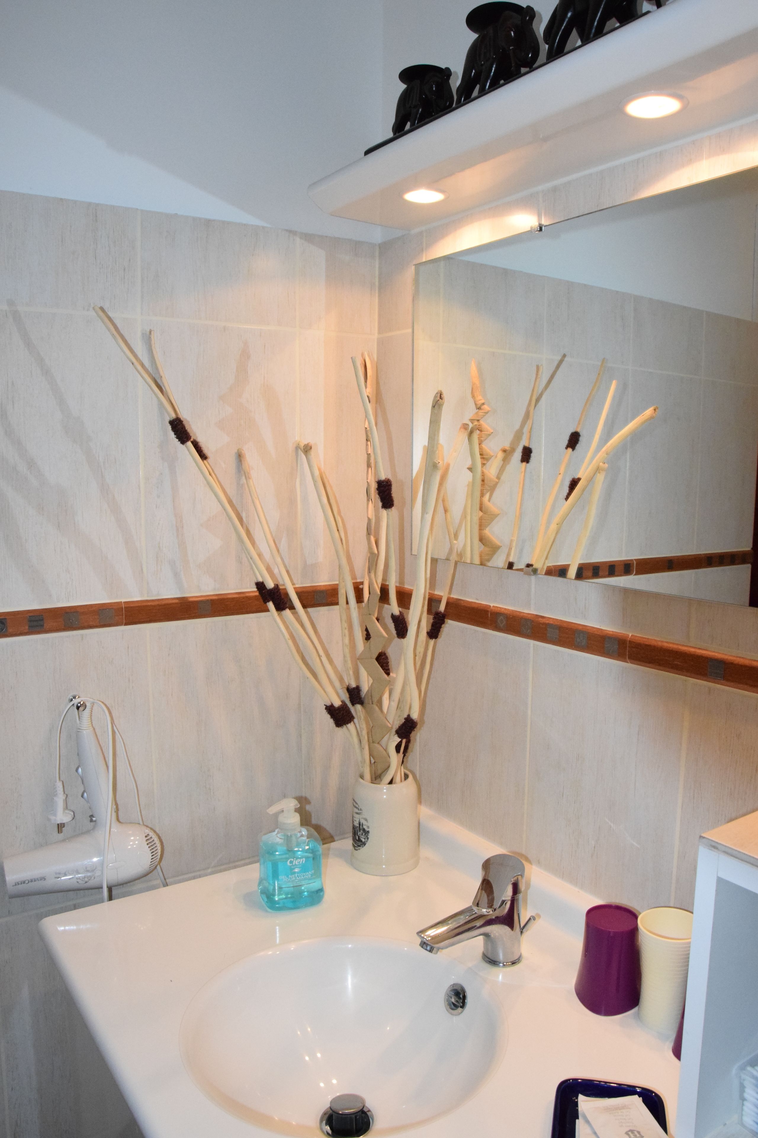 A bathroom with a white sink, a mirror, a bottle of hand soap, and a cup.
