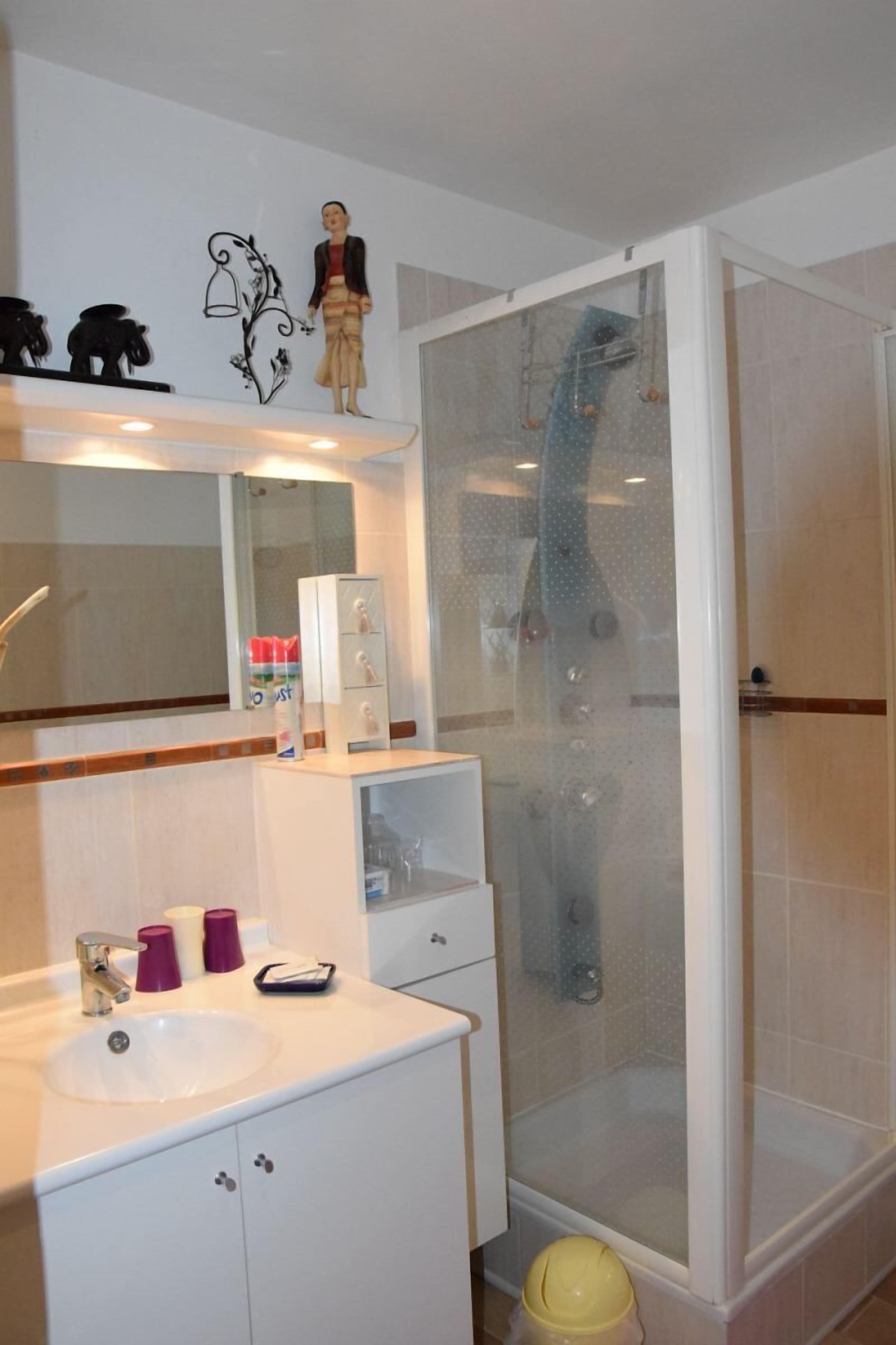 Uma casa de banho com uma pia branca, espelho e cabine de chuveiro com vidro.