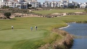 Ein Golfplatz mit einem Wasserhindernis und Gebäuden im Hintergrund.