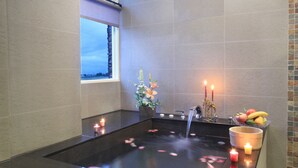 A modern bathroom with a black bathtub, a window, candles, and a fruit bowl. - Spring Fountain Hotel (Jiaoxi)