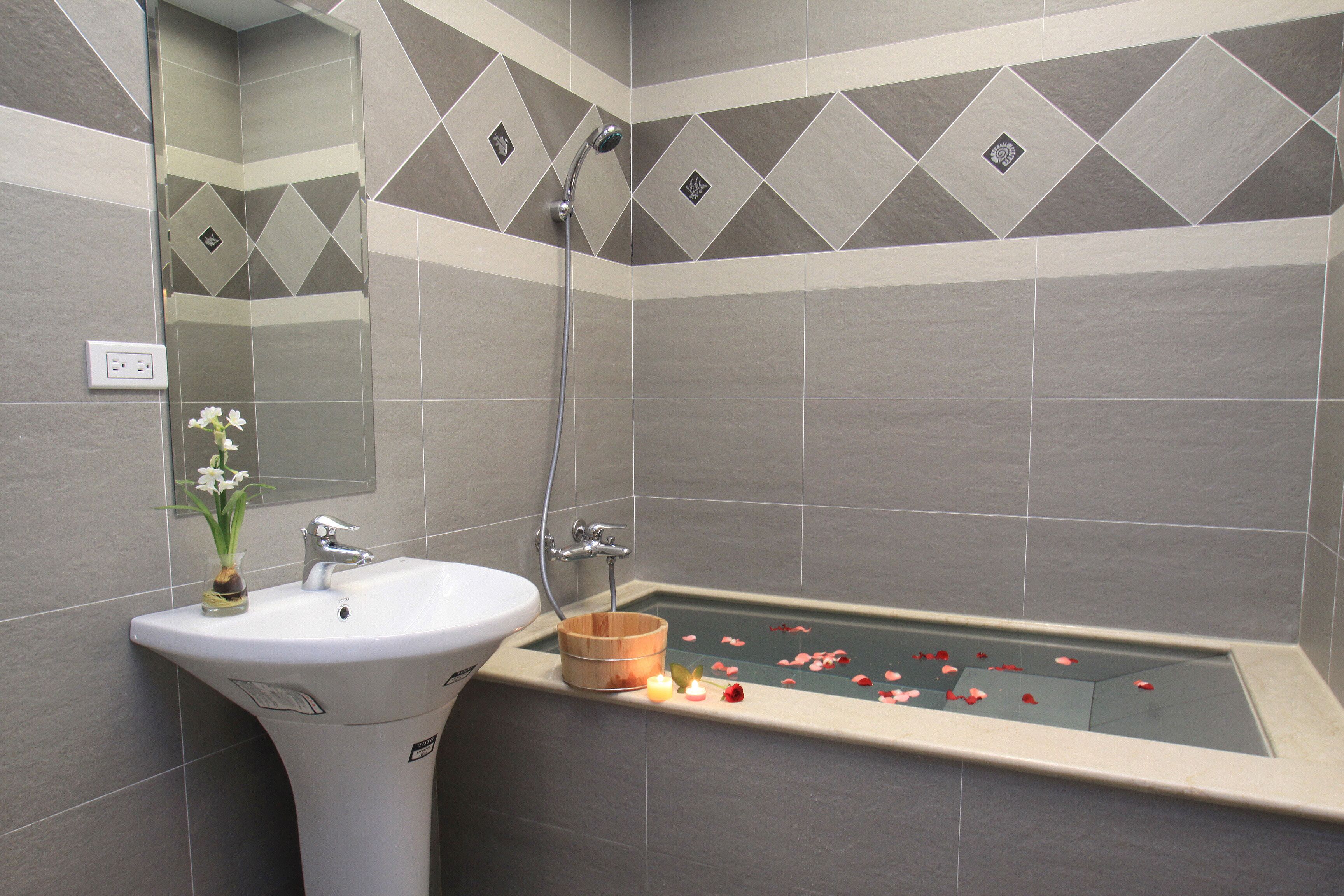 Un baño con lavamanos, espejo, ducha y bañera con pétalos de rosa.