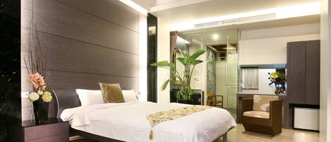 A modern bedroom with a large bed, bedside tables, a chair, and a plant.