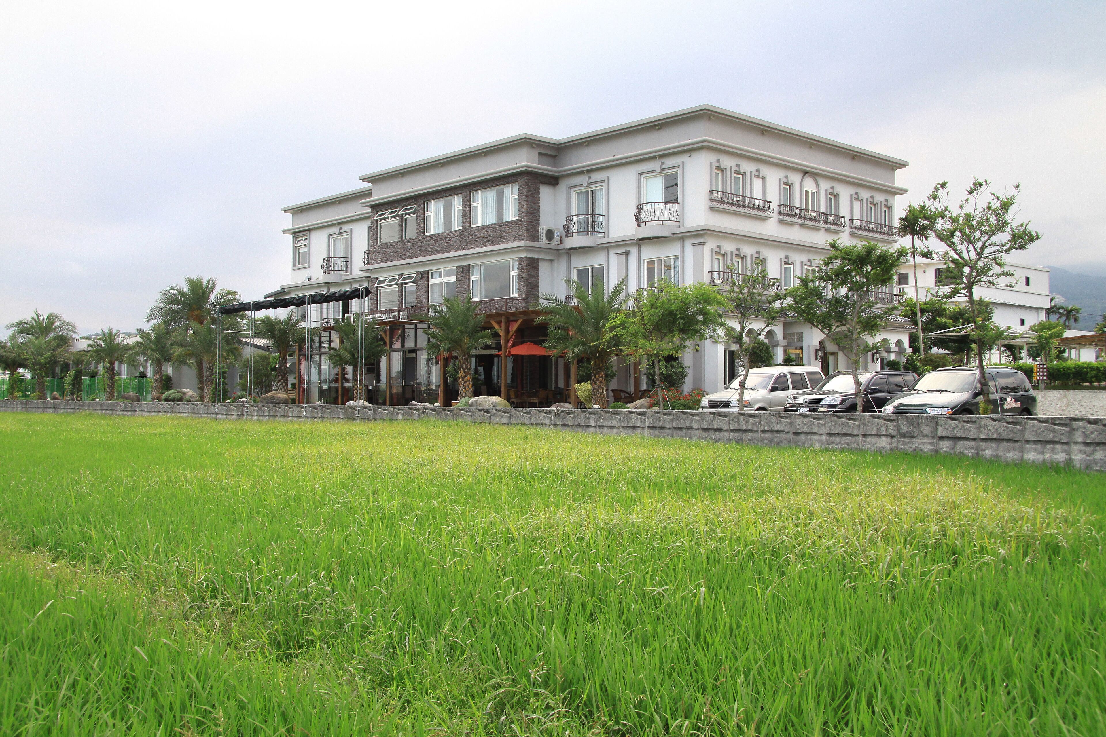 A multi-story hotel with a large entrance, a covered outdoor area, and a parking lot with several cars.