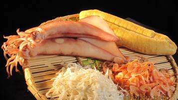 Un plateau en bambou garni de calamars coupés en tranches, d’une banane, de légumes râpés et d’une portion de nouilles.