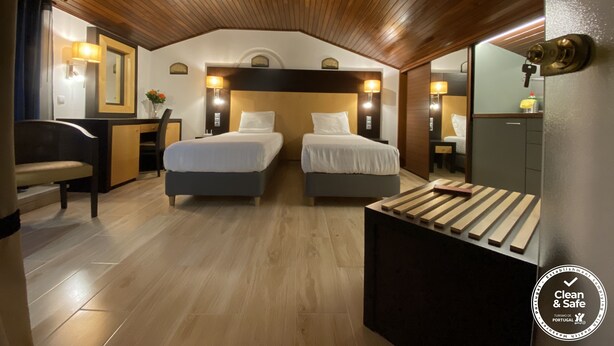 A hotel room with two beds, wooden ceiling, and a desk with a chair. - Discovery Apartment Carnaxide (Oeiras)