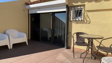 Ein Balkon mit einer Schiebetür aus Glas, zwei weiße Kunststoffstühle und einem kleinen runden Tisch mit Metallstühhlen.