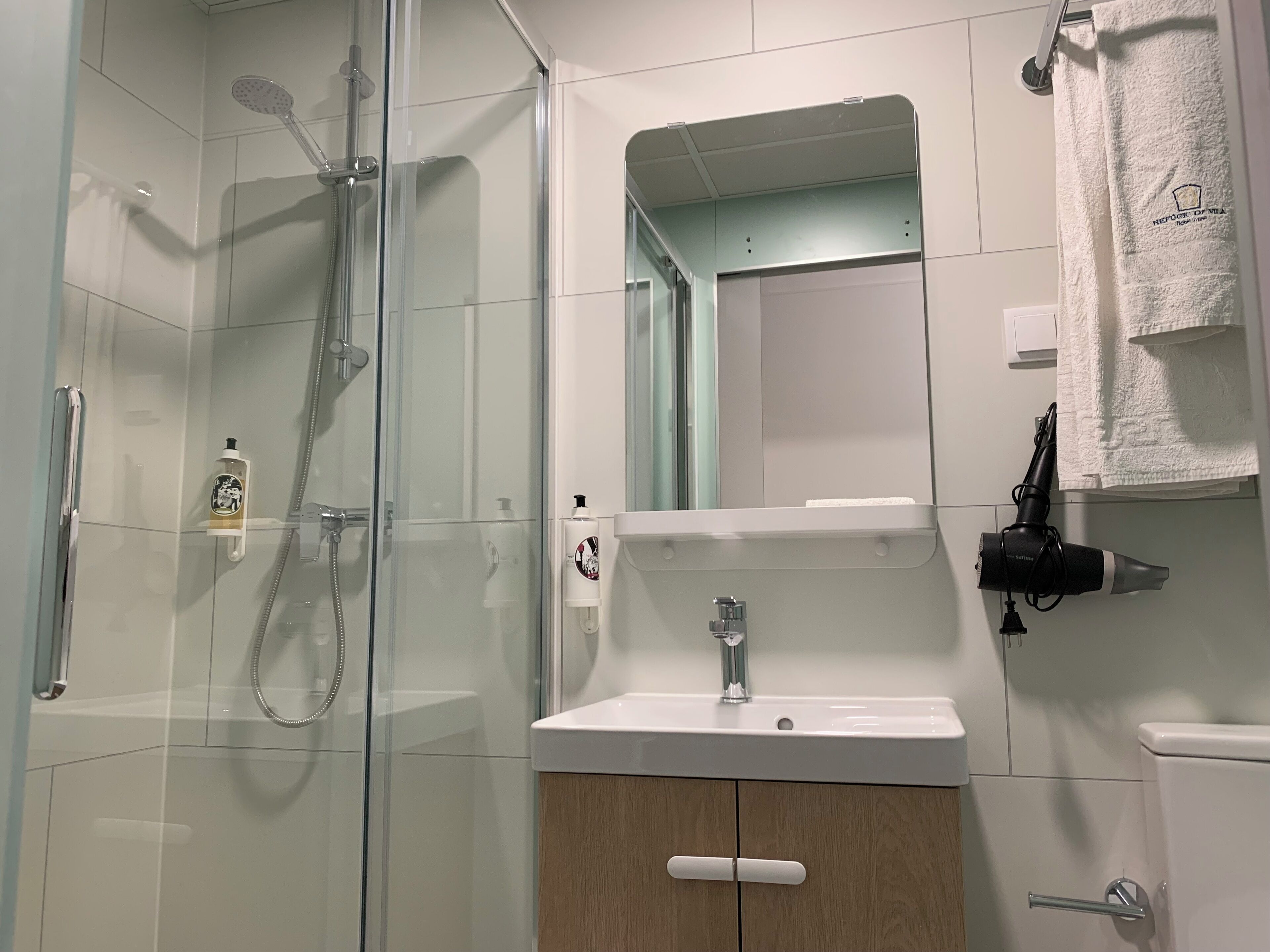 Un baño moderno con ducha de vidrio, un lavamanos blanco y un espejo sobre él.