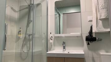 Un baño moderno con ducha de vidrio, un lavamanos blanco y un espejo sobre él.