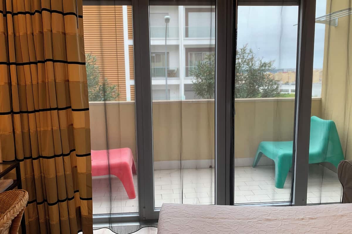 Ein Zimmer mit einer großen Schiebeglas-Tür, die auf einen Balkon mit zwei Stühlen und einem Tisch im Freien führt.