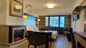 A hotel room with a fireplace, a bed, a dining table, and a TV mounted on the wall. - Discovery Apartment Carnaxide (Oeiras)