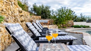 A poolside area with lounge chairs and two glasses of orange drink on a table. - Amazing home in Kucine (Kucine)
