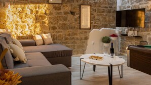 A cozy living room with a stone wall, a sofa, a coffee table, and a television. - Amazing home in Kucine (Kucine)