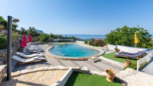 A pool area with lounge chairs and umbrellas, surrounded by stone walls and greenery, overlooking a scenic view. - Amazing home in Kucine (Kucine)