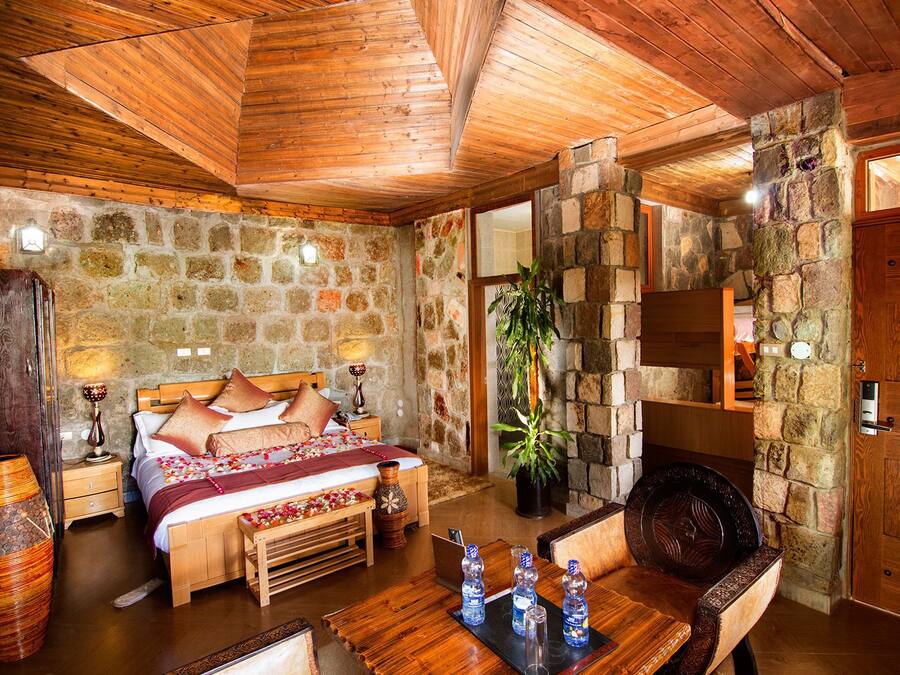 Une chambre confortable avec un mur en pierre, un plafond en bois et un lit agrémenté d’oreillers et d’une couverture.