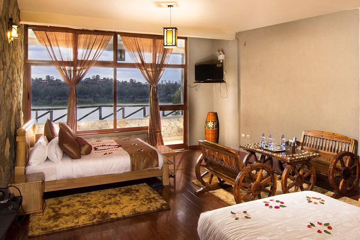 A room with a bed, a wooden table, and a view of a lake.
