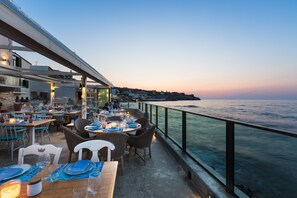 An outdoor dining area with tables set for a meal, overlooking a body of water and a distant shoreline. - Thalassa Boutique Hotel - Adults Only (Rethymno)