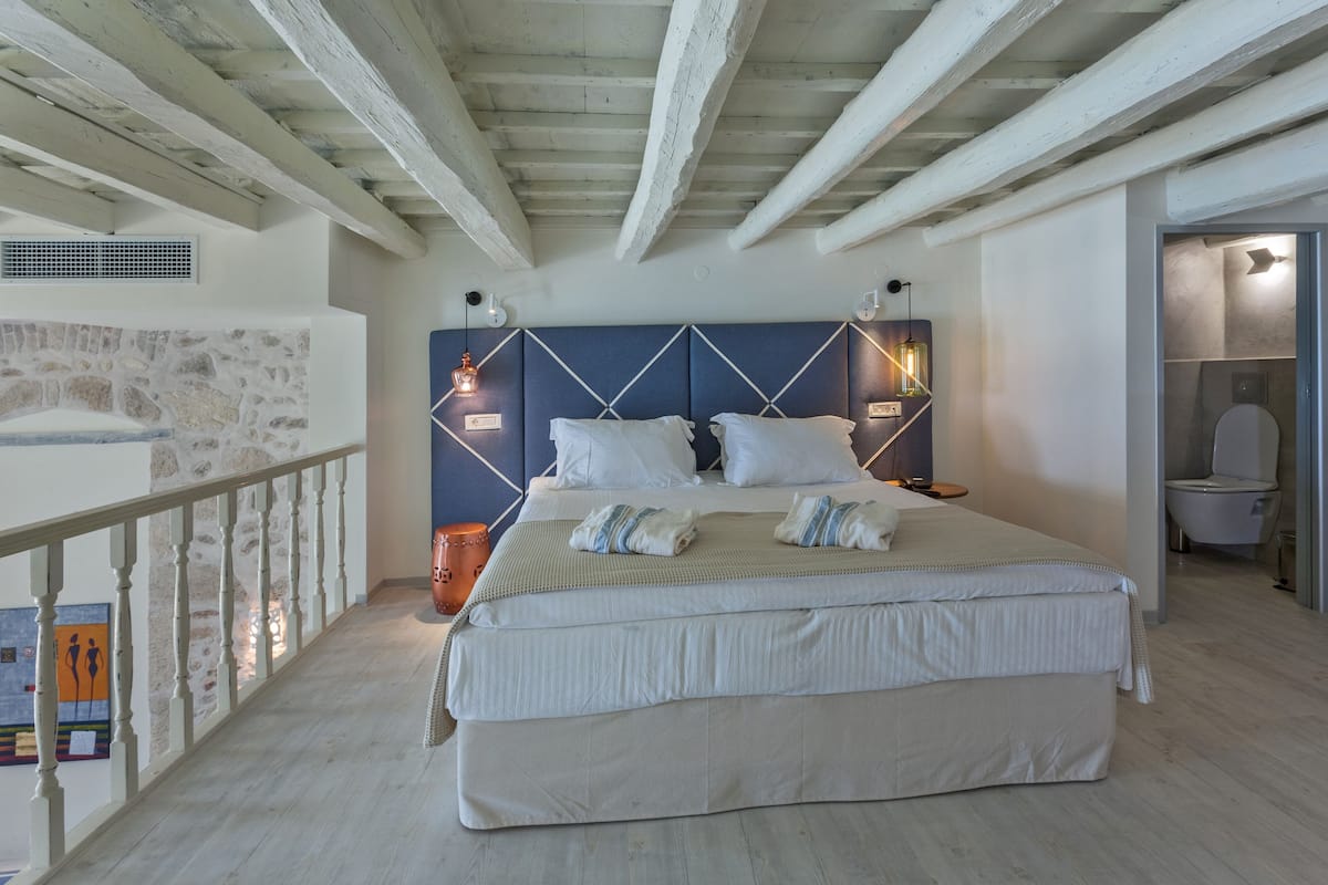Un dormitorio con una cama grande, pared de piedra, balcón y baño.