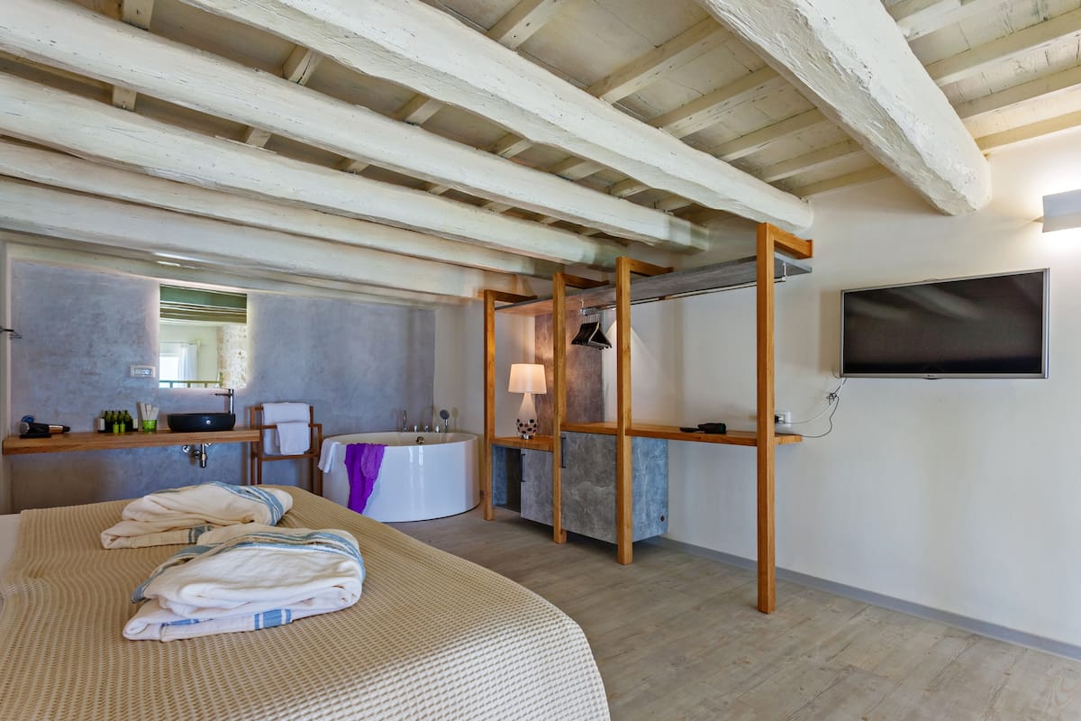 Un dormitorio con una cama grande, una bañera, techo de madera y un televisor montado en la pared.