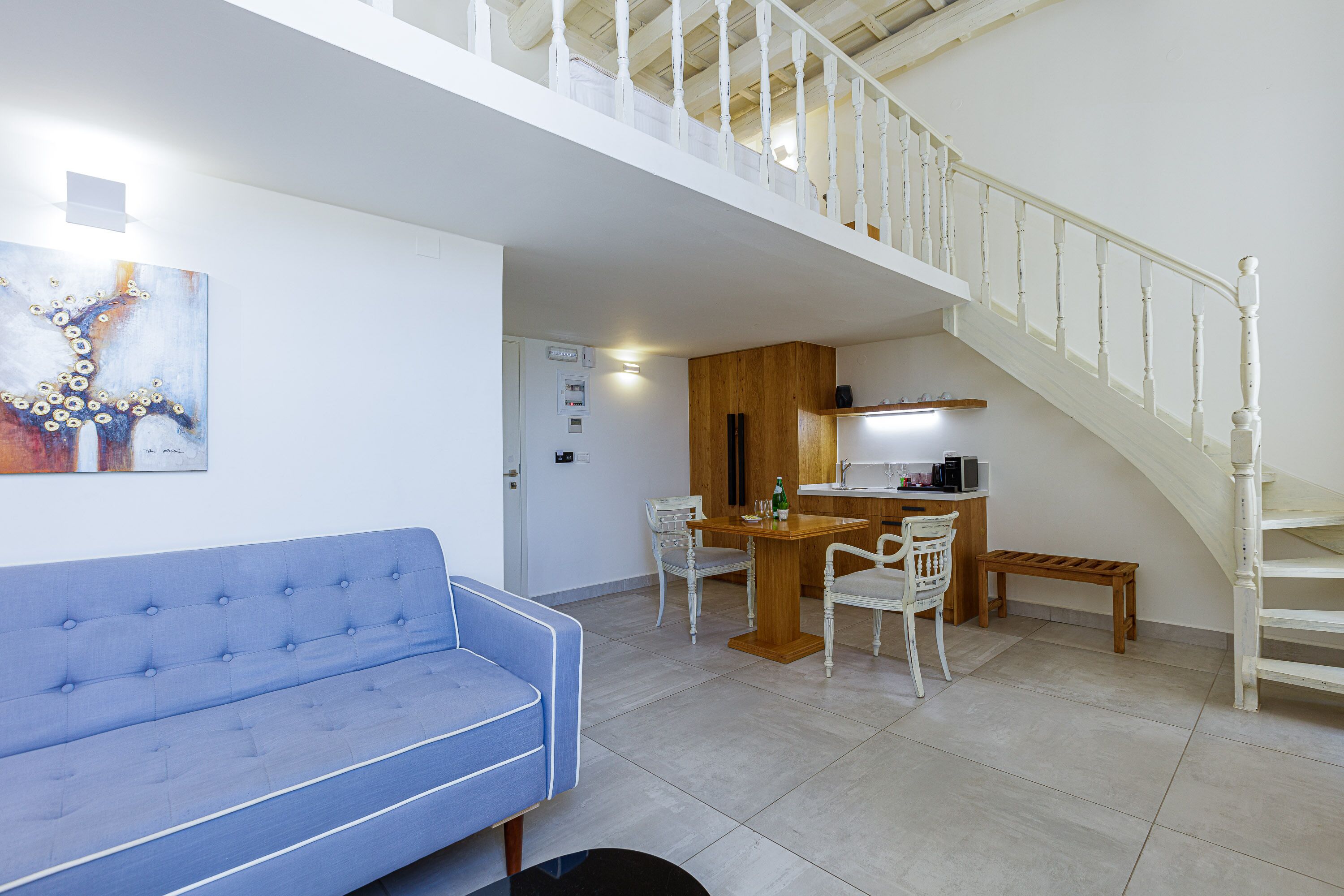 Amplia sala de estar con un sofá azul, una mesa de comedor de madera con sillas y una escalera.