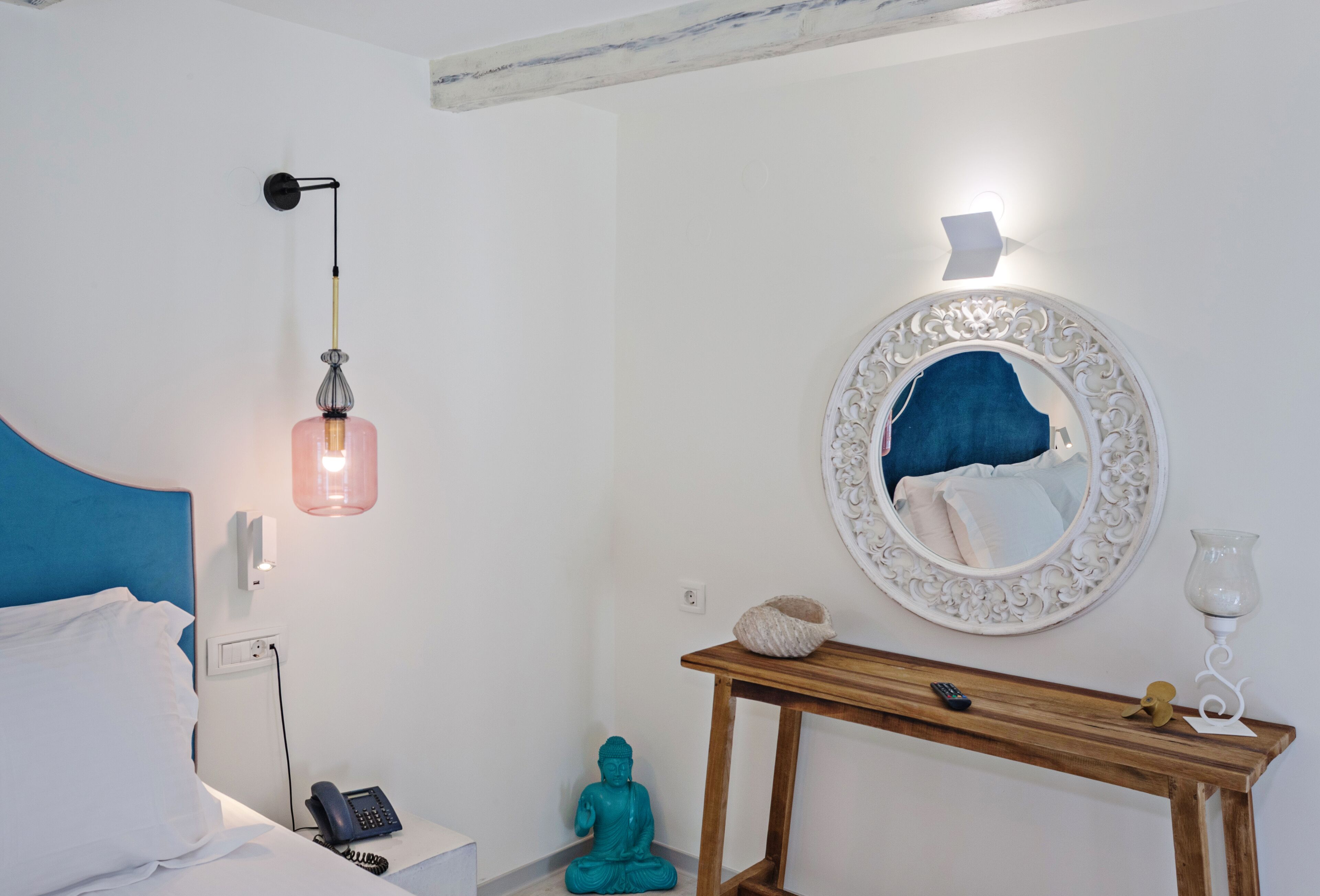 A bedroom with a bed, bedside table, lamp, mirror, and a small Buddha statue.