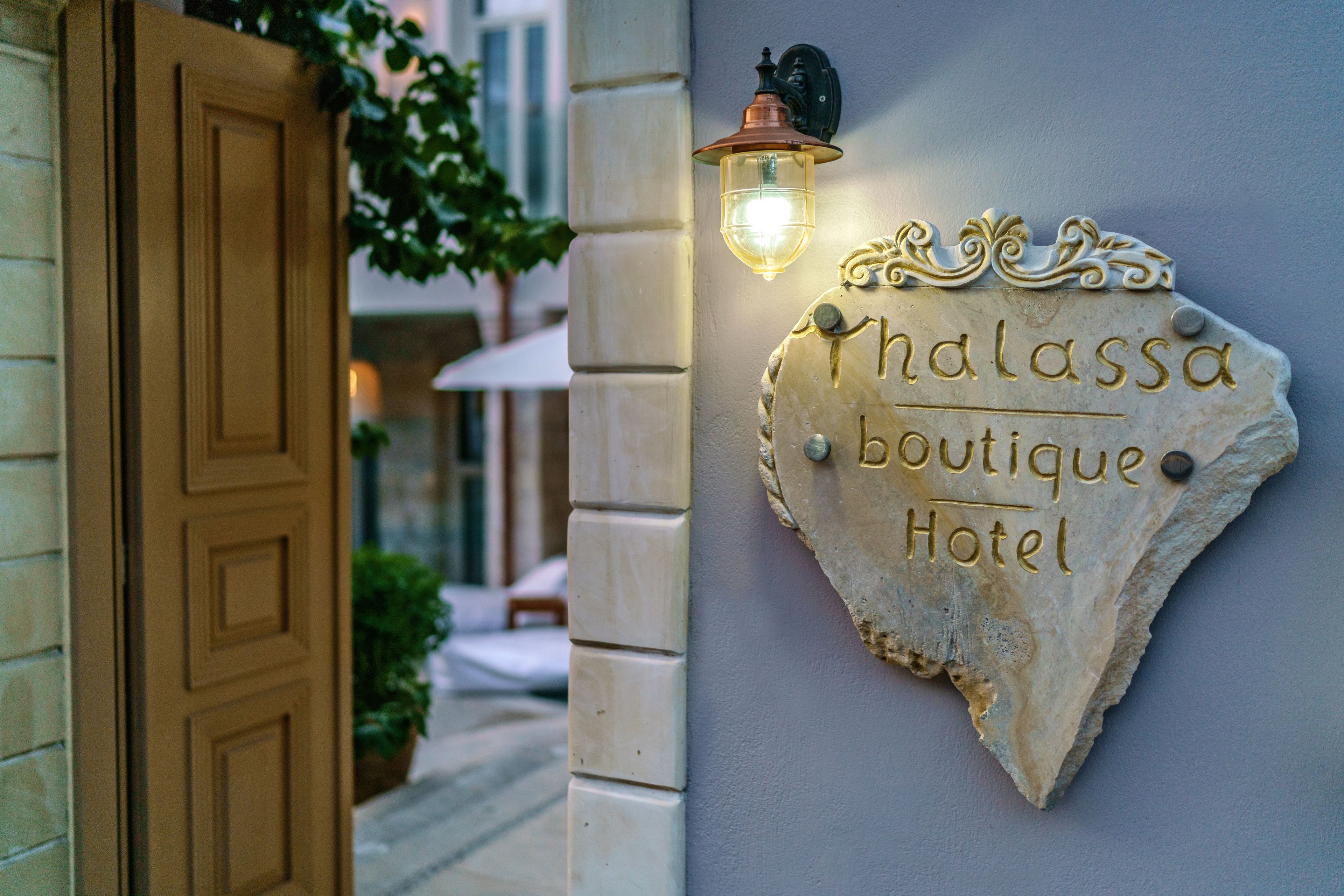 Une enseigne indiquant « Thalassa Boutique Hotel », avec un luminaire décoratif placé au-dessus.
