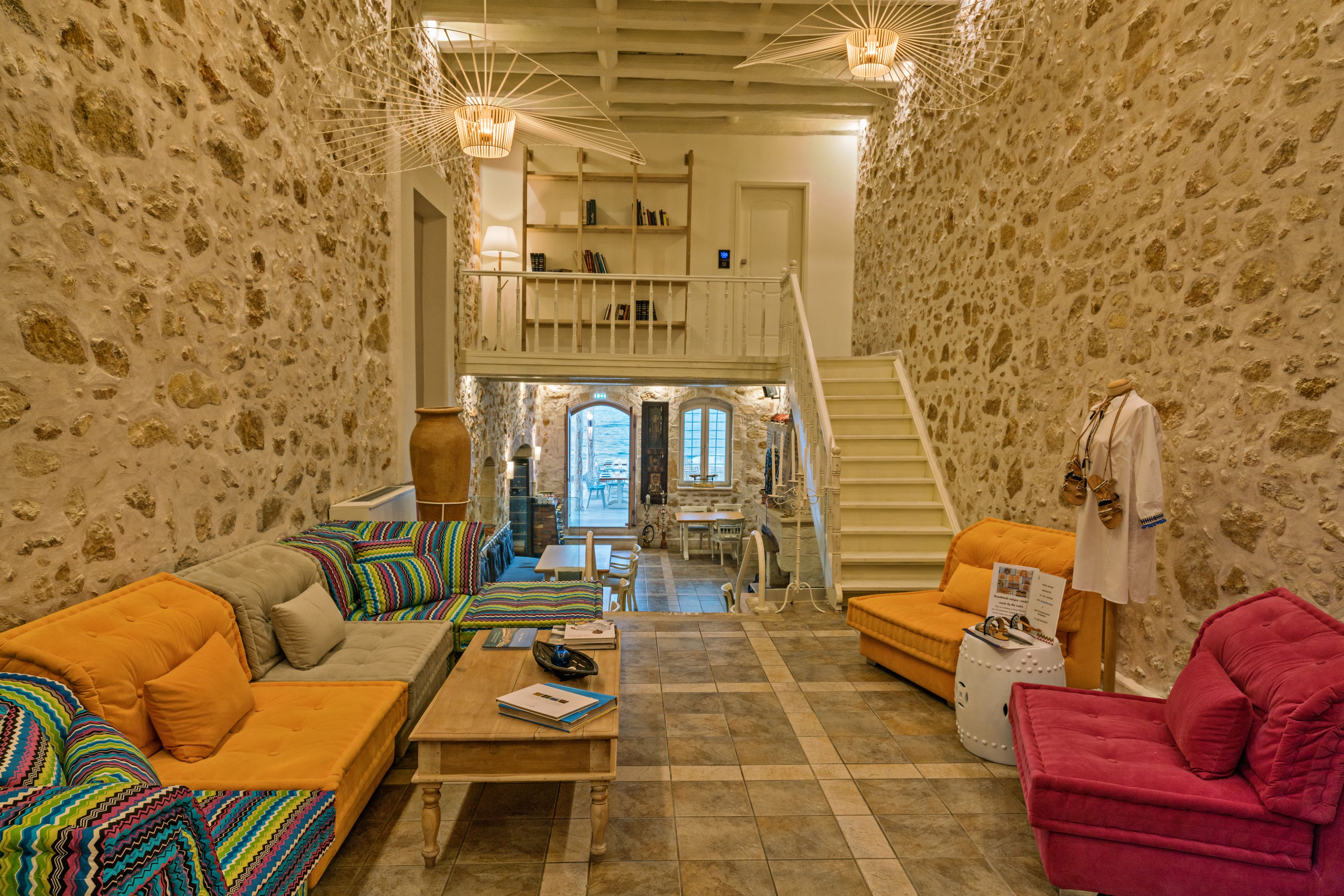 A spacious living area with a stone wall, a staircase leading to a loft, and a view through a window.