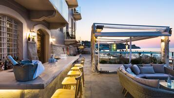 A bar area with a long counter, yellow chairs, and a wicker sofa under a pergola.