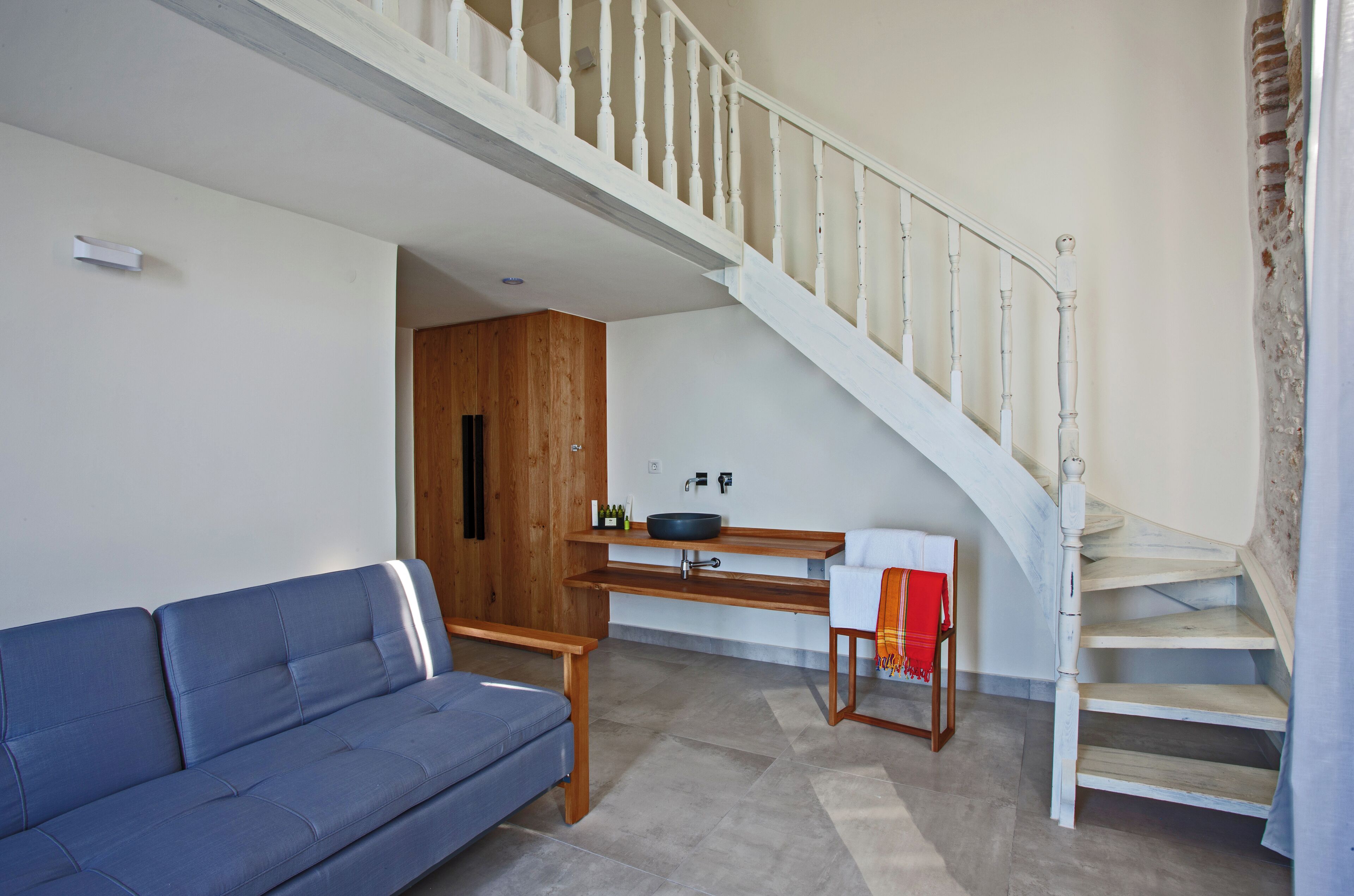 A living room with a blue sofa, wooden bench, and a white staircase.