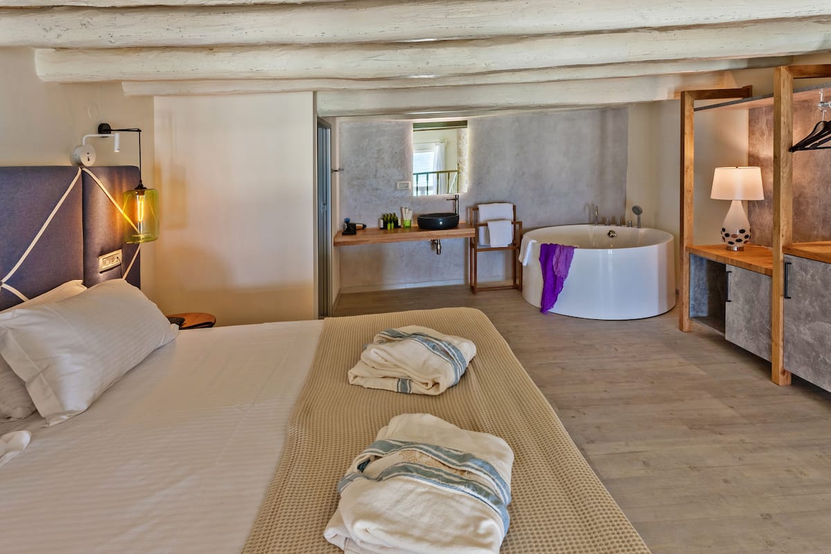 Una habitación de hotel con cama, baño con bañera y estante de madera con lámpara.