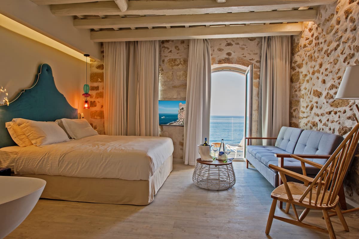 Un dormitorio con cama, sofá, sillón de mimbre y vista al mar.