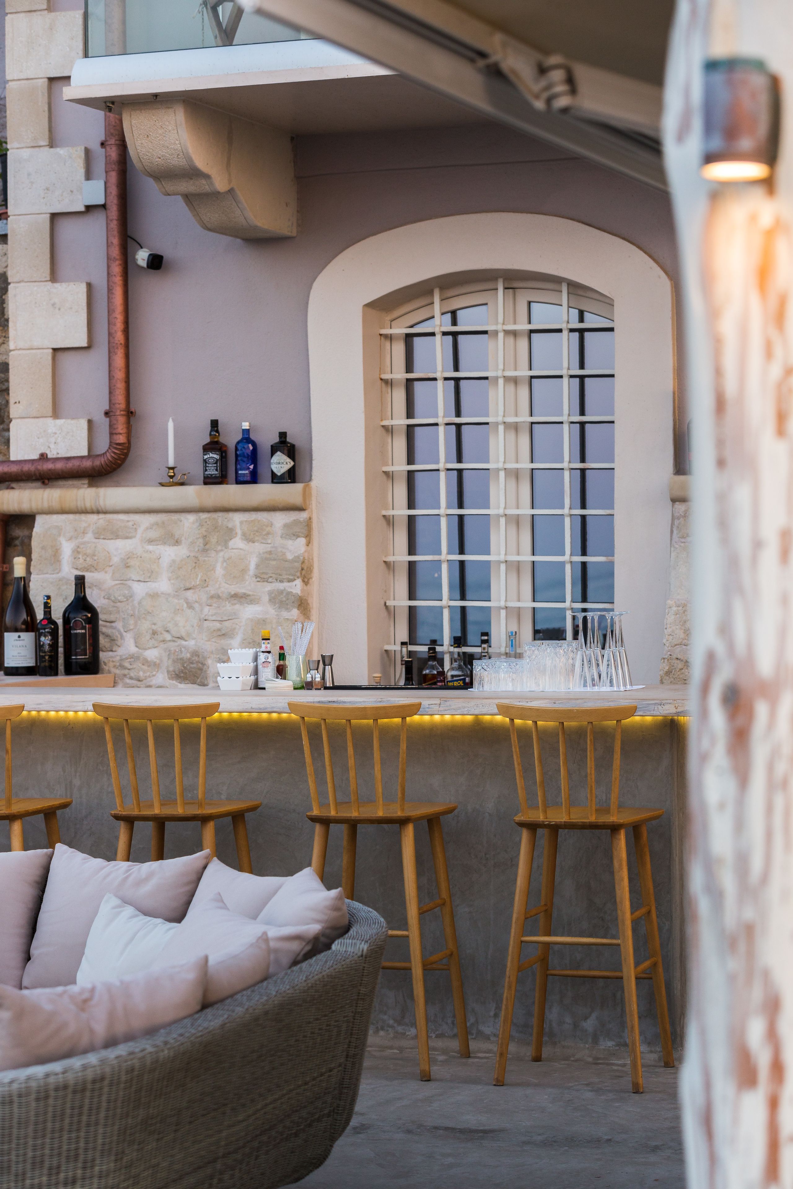 Una zona de bar con paredes de piedra, sillas de madera y un sofá de mimbre.