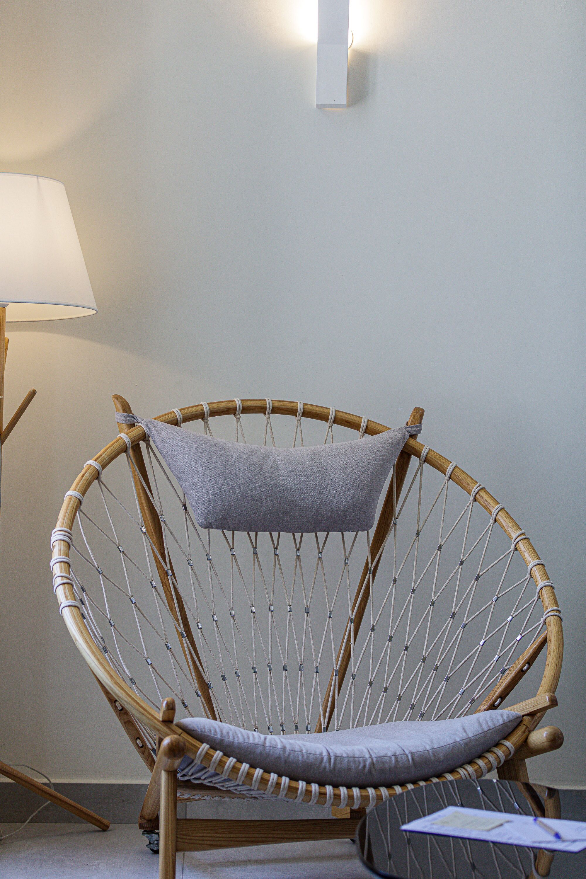 Une chaise en osier avec un coussin, placée près d’un luminaire fixé au mur.